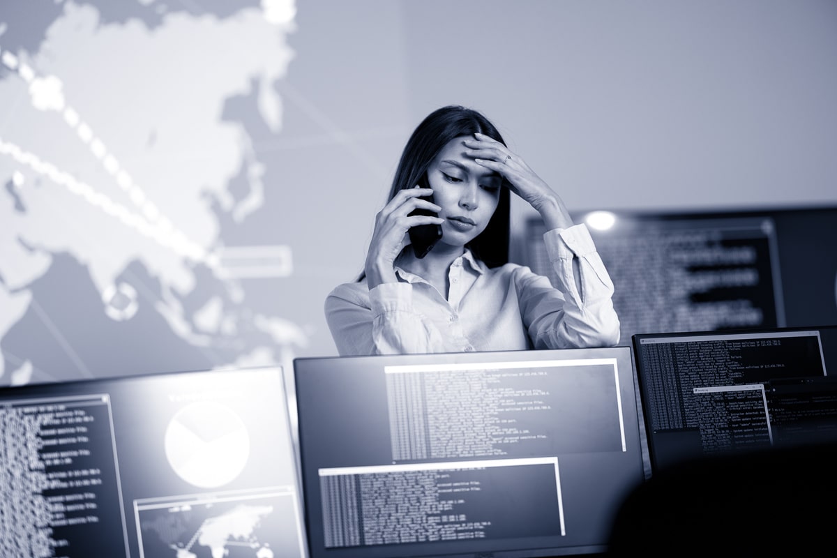 Focused and concerned confident female Cyber Security Analyst or Manager in enterprise Security Operations Center (SOC). A team of security operators resolving a critical cybersecurity breach.